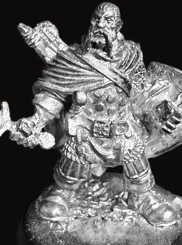 An unpainted pewter miniature of Garrin Vosk — a bearded warrior pointing forward with one hand, a longsword held low in the other, a large kite shield on his arm, wearing layered scale and cloth armor and a cloak, standing on a rocky round base