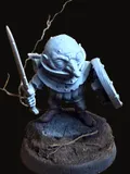 An unpainted miniature of Rollo — a small svirfneblin with a wide bald head and oversized ears, sword raised in one hand and a round shield held at the ready in the other, standing in a battle-ready crouch on a dark textured round base