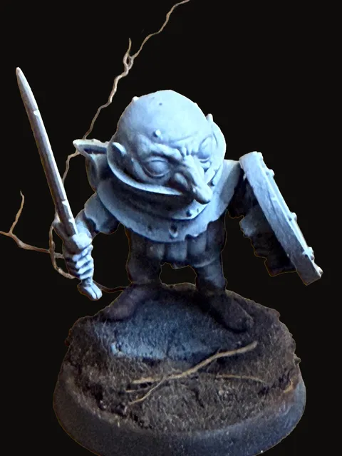 An unpainted miniature of Rollo — a small svirfneblin with a wide bald head and oversized ears, sword raised in one hand and a round shield held at the ready in the other, standing in a battle-ready crouch on a dark textured round base