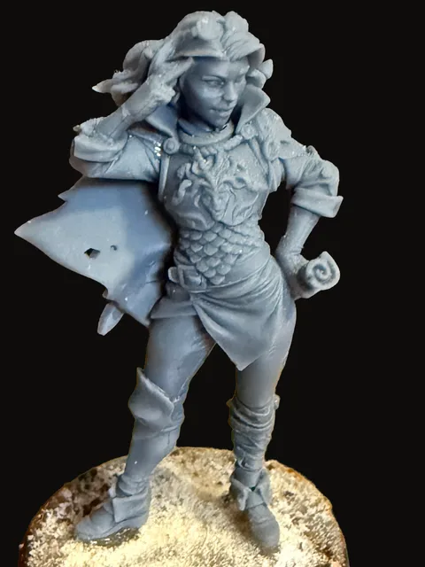 An unpainted resin miniature of Triste — a slender feminine figure in a flowing cloak and dress, long hair falling over one shoulder, standing on a textured round base